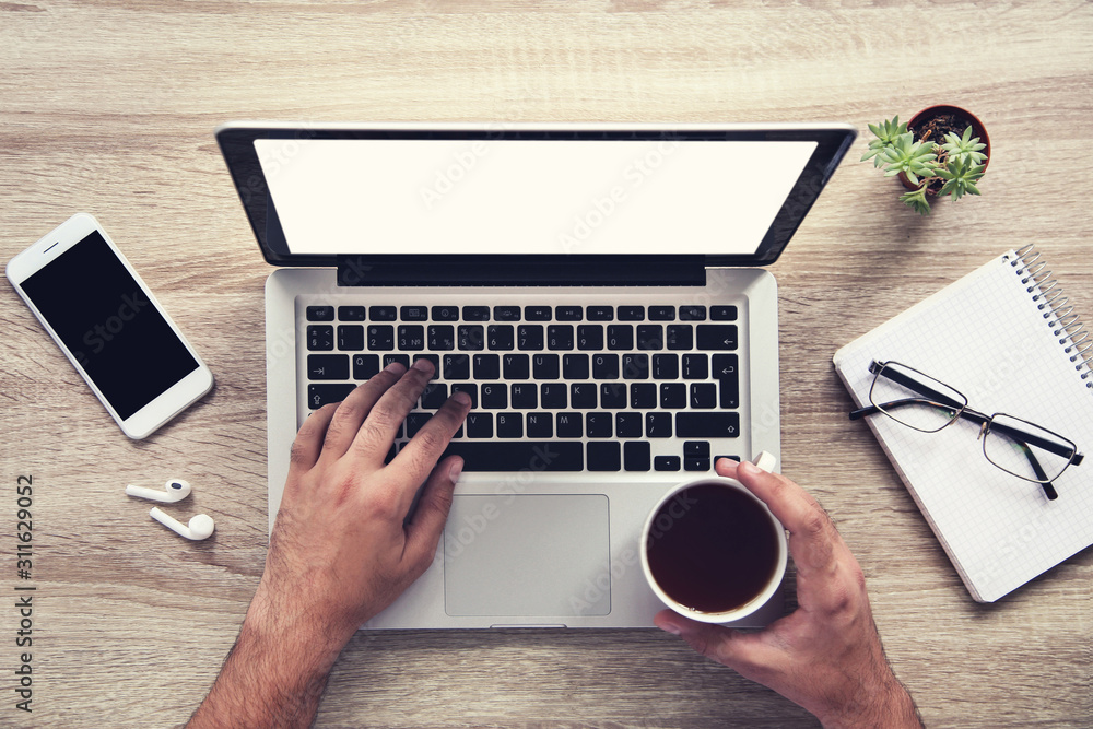 Poster man working on laptop computer with cup of tea, smartphone and notepad in the office
