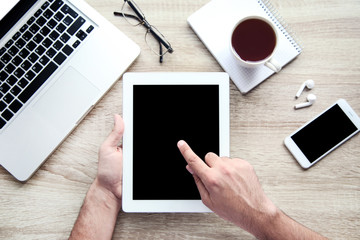 Male hands holding tablet computer with laptop, smartphone and cup of tea on table