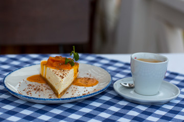 Mandarin topping cheesecake and cup of coffee on table in daylight