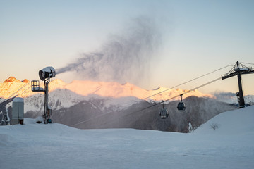 Obraz premium Snow cannon on the background of evening mountains and cable car. Preparation for the ski season.