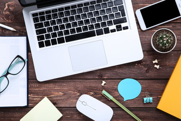 Laptop computer with office supplies and smartphone on brown wooden table