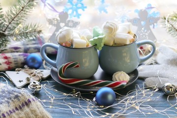 Two cups with a drink, marshmallows, caramel sticks, Christmas decor, illuminations on a wooden surface on a window background,  winter holidays, blue color
