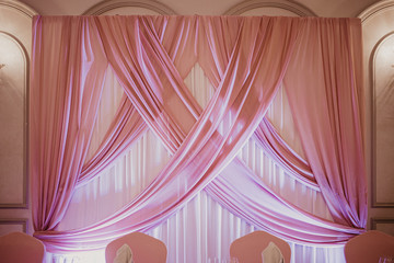 Wedding pink decoration in the restaurant. Pink fabric wall over the table of wedding couple