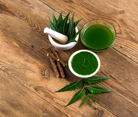 Medicinal Neem leaves in mortar and pestle with neem paste, juice and twigs on wooden background