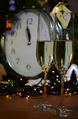  Two glasses of champagne against the background of the clock, which show midnight and the beginning of the New Year