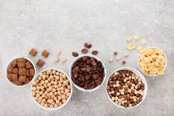 Various corn flakes in bowls on grey background