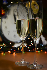 Two poured glasses with champagne against the background of a garland and a clock, which will now show the onset of the New Year 2020