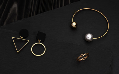 Fototapeta na wymiar Geometric design golden earrings, pearl bracelet and ring on dark background
