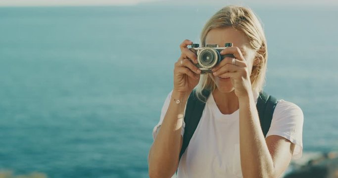 Portrait of an attractive young woman smiling and taking a picture with her vintage camera, happy traveler woman on a hike taking a photograph