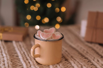 Homemade cocoa with marshmallows in an iron mug on a background of blurry lights.