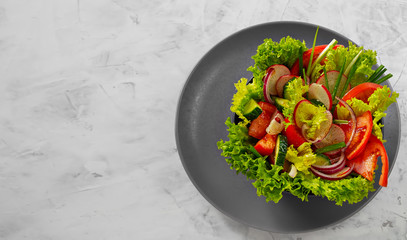 Fresh vegetable salad in a white cup on a gray dish. View from above. Copy space. Light gray background.