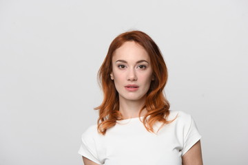 The face of a beautiful woman with red hair a little lower than the shoulders. In a light dress with short sleeves, she has a confident, friendly look in which determination and humility are manifeste
