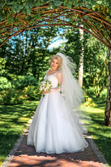 Obraz na płótnie Canvas Beautiful blonde bride stands near the arch in greenery. Wedding portrait of a cute bride with a bouquet in the scenery. Concept and photography.