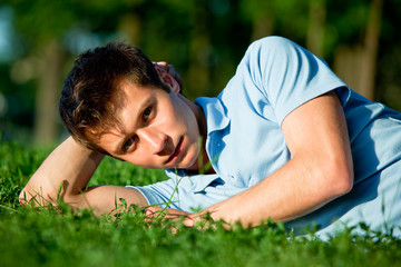 Naklejka na ściany i meble Young man in casual clothing lying on green grass and looking at camera