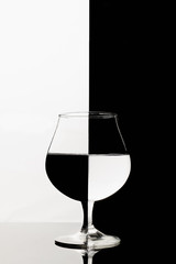 A half full cognac glass with interesting refraction effect on black and white background.