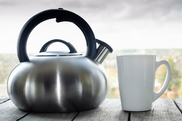 Steel tea kettle and mug. Hot morning tea in clay white mug and kettle on wooden breakfast table