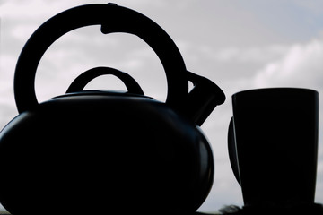 Naklejka na ściany i meble Steel tea kettle and mug. Hot morning tea in clay white mug and kettle on wooden breakfast table