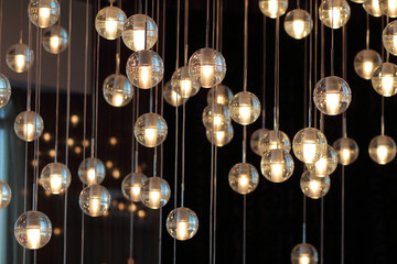 Obraz premium lighting balls on the chandelier in the lamplight, light bulbs hanging from the ceiling, lamps on the dark background, selective focus, horizontal
