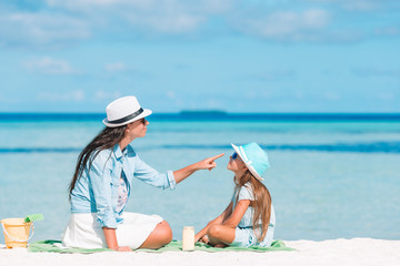 Young mother applying sun cream to daughter nose on the beach. Sun protection