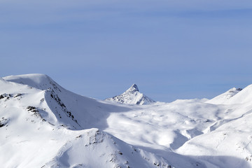Fototapeta na wymiar Snowy off piste ski slope, sunlit plateau and peak at high winter mountains