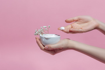 open jar of body cream or face cream in female hands on a pink background, the girl moisturizes the skin