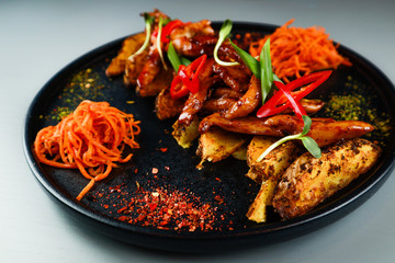 Chicken fillet in Asian teriyaki sauce. Carrots. Baked potatoes. Black plate. Gray background. Restaurant