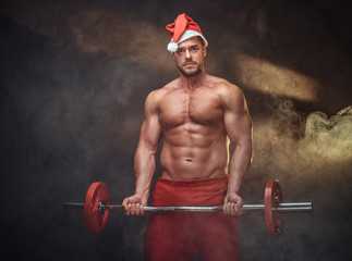 Fototapeta na wymiar Portrait of shirtless man in Santa costume with barbell in hands.