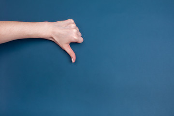 Female hand shows thumb down on blue background, place for text