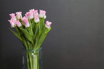Glass vase with pink tulips on a dark wooden table, greeting background or concept