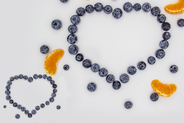 A heart's frame from mandarin pieces and blueberry on white background. A composition of the mandarin pieces and berries in form a heart. Beautiful frame and full of the vitamins