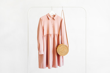 Pale pink dress with bamboo bag on hanger on white background. Elegant   fashion outfit. Spring...
