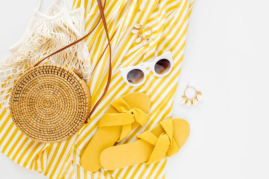 Yellow dress with stripes with slippers, sunglass, and bamboo bag. Women's stylish summer outfit. Trendy clothes. Flat lay, top view.