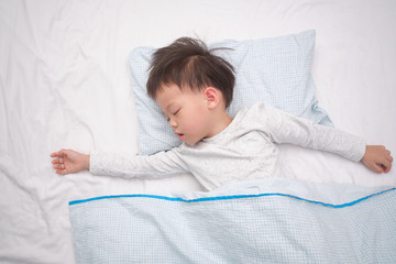 Cute little Asian 3 - 4 years old toddler boy kid in pajama taking a nap, sleeping on his back on white bed sheet in bed, Bedtime for kids concept with copy space