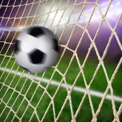 A ball flying in the goal net with a green field and lights on a background