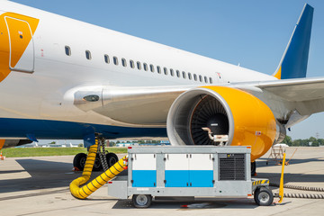 Big modern commercial plane parked on airport runway and connected to ground supply power unit. Aircraft maintenance service and check-up before flight. Airport handling industry