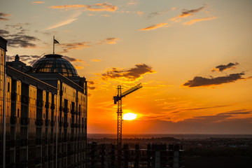Dark Silhouette of construction crane and building from glass on sunset sky background. Used for...