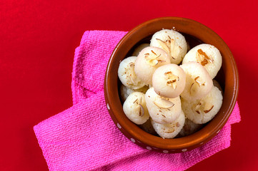 Indian Sweet or Dessert - Rasgulla, Famous Bengali sweet in clay bowl with napkin on Red Background