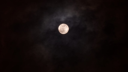 Naklejka na ściany i meble Close-up of full moon isolated on dark blue sky with light clouds, telephoto image.