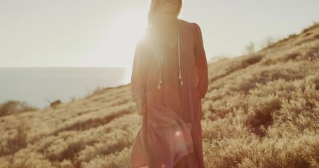 Beautiful artsy bohemian woman smiling and enjoying herself at sunset by the ocean, fashion modeling at sunset