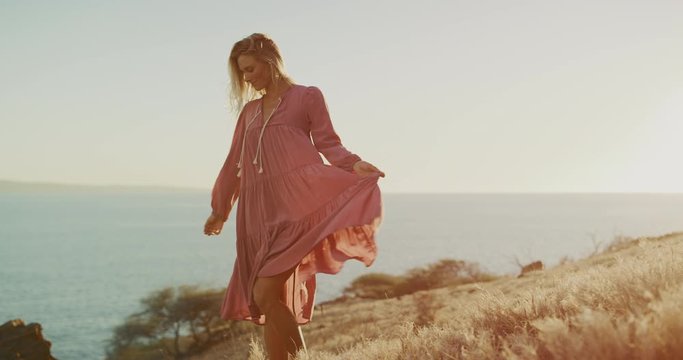 Young attractive fashion model dancing in a golden field at sunset, happy carefree woman in a flowy dress dancing at sunset by the ocean