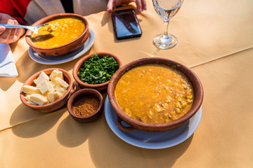 Woman eating locro, typical Argentine food, accompanied by bread and a glass of wine, with spoons.