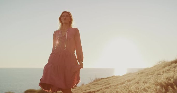 Young happy woman posing in a pink flowy summer dress at sunset with golden sun flare, artsy fashion model posing for the camera, gorgeous bohemian fashion moments