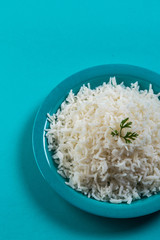 Cooked plain white basmati rice with corriander in a blue plate on blue background