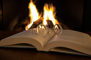 close up of vintage eyeglasses on open book with fireplace background