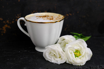 Cup of frothy coffee (cappuccino) and white flowers. Coffee time, romantic breakfast.