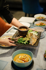 A woman's hand holding a vegetable dish and fried mackerel with chili paste paste