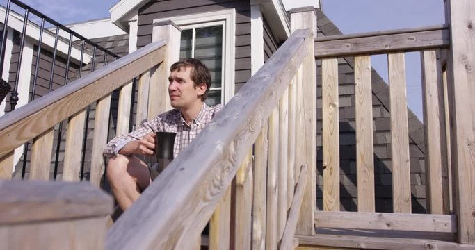 Man in 20s sips morning coffee outdoors on rooftop patio overlooking city