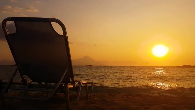 Greece, sandy beach in sunrise. Steady shot of the perfect waves crashing in the beach with a sun luger in the shadow