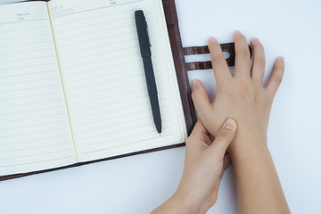 Closeup woman massaging her painful hand with notebook and pen background. Healthcare concept. Health care and medical concept.