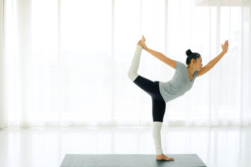 Fototapeta premium Side view of Beautiful Asian woman practicing yoga, standing in Natarajasana exercise, Lord of the Dance pose, working out, wearing sportswear,full length,indoor,lifestyle healthy concept.